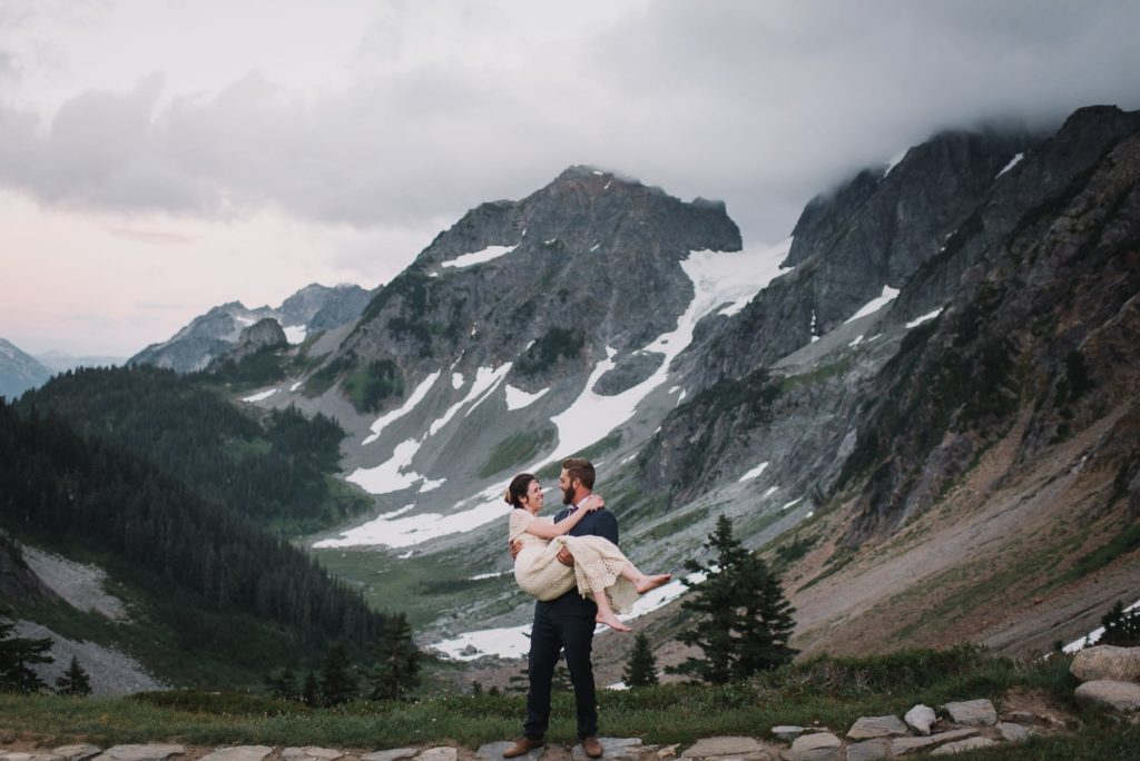 groom holding bride with mountains in the background
