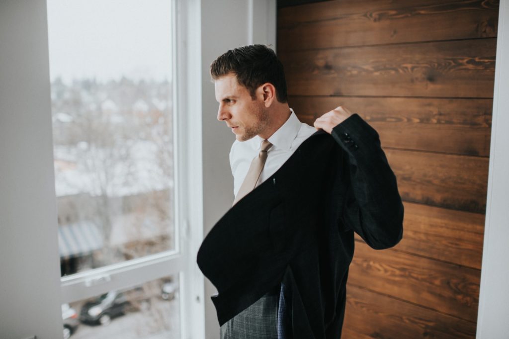 groom putting on his jacket by the window