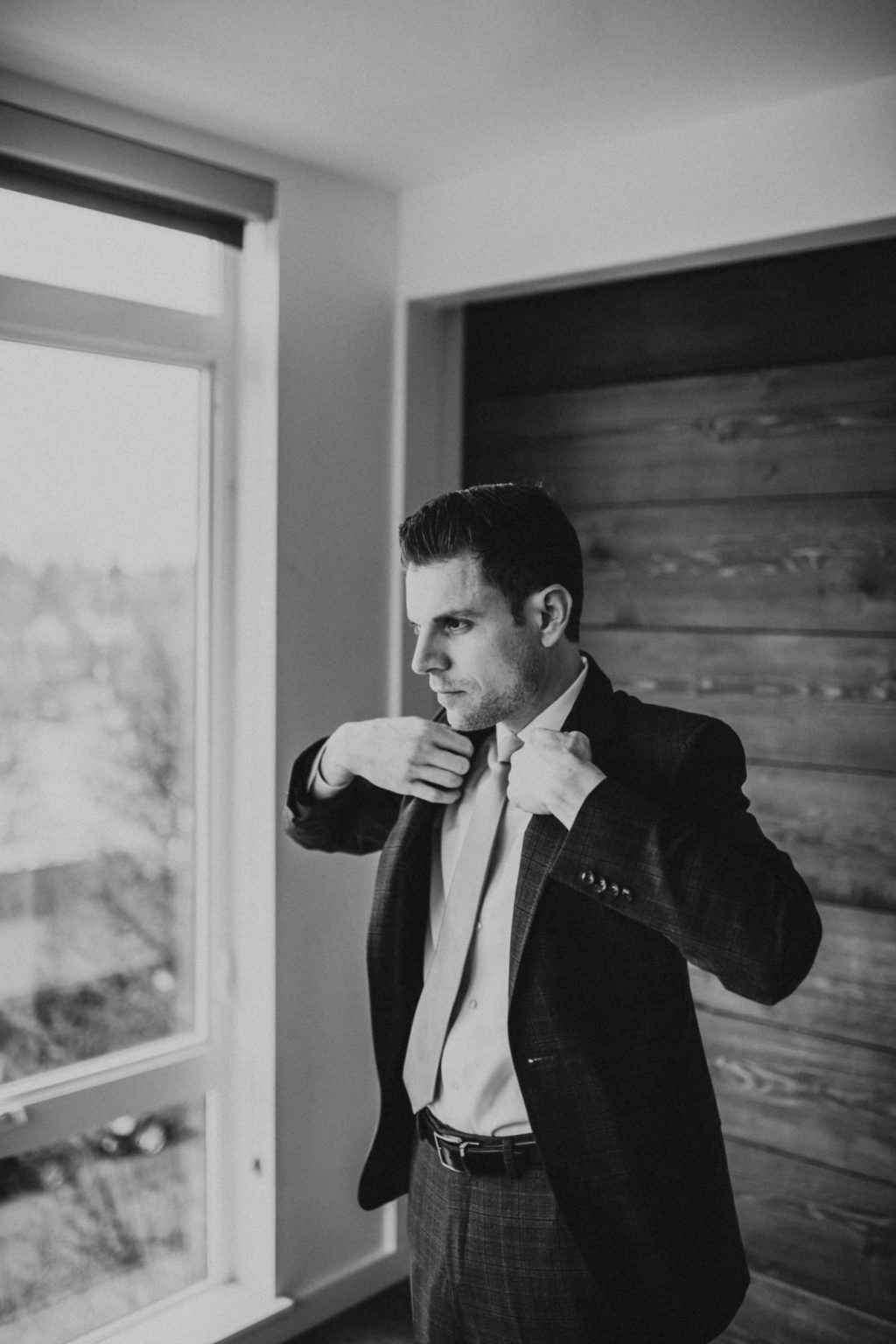 black and white of groom putting on jacket