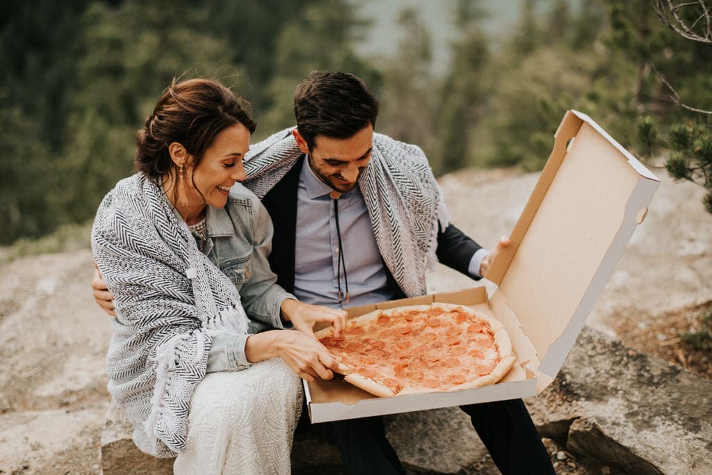 bride and groom sharing pizza on top of a mountain