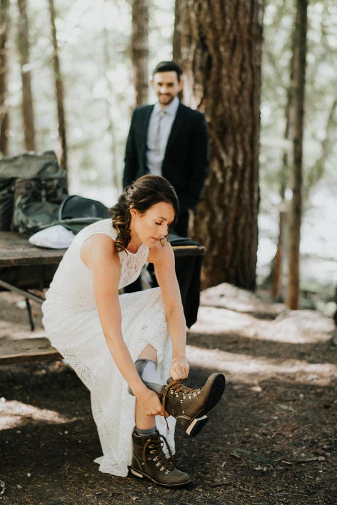 bride putting on hiking boots at campsite