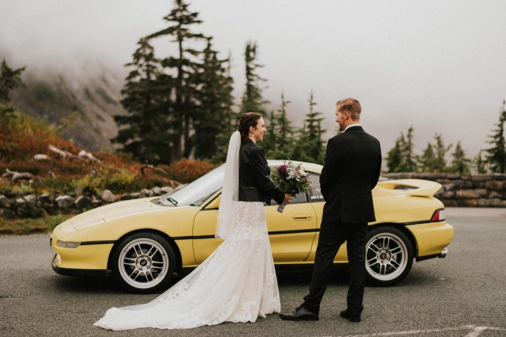 bride and groom standing in front of car
