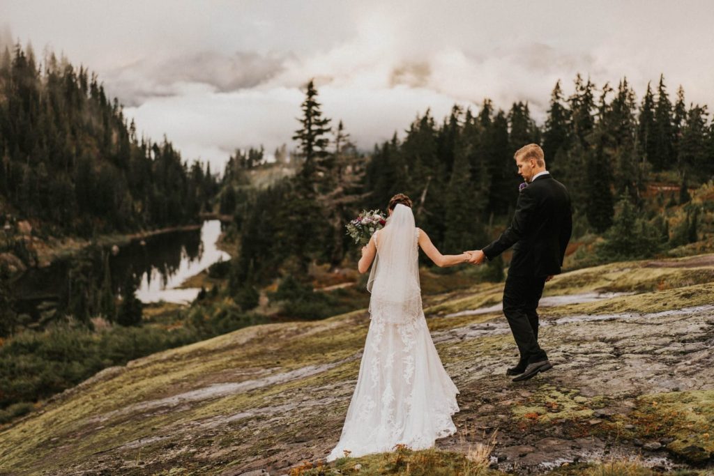 bride and groom walking toward alpine lake
